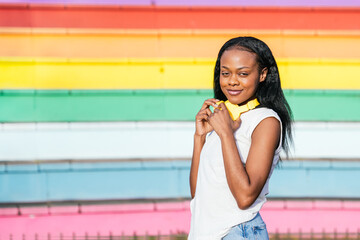 Joyful black woman in casual attire against vibrant LGBT wall.