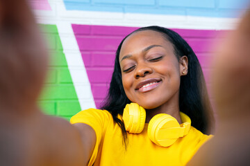 Cheerful afro lady captures a selfie with a multihued wall behind