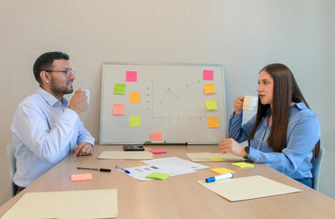 A man and woman sitting at a table with a white board and sticky notes