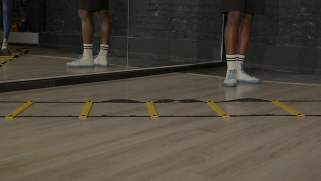 Close-up of human legs practicing cardio intense workout using agility ladder for footwork training, doing side straddle hop exercise, improving coordination and quickness indoors.