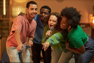 Diverse group of adult friends singing to microphone together and enjoying karaoke together at house party