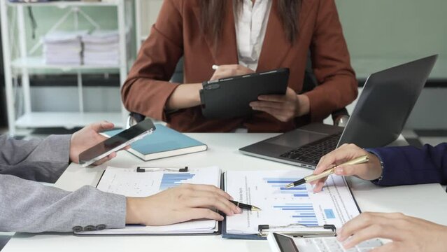 A multicultural team of professionals, including male and female businesspersons, convenes around a desk with tablets, discussing strategies illustrated on a whiteboard during a dynamic presentation.