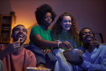 Multiethnic group of excited young people watching comedy movie together in dark room