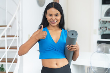 Motivated hispanic woman with yoga mat ready for class at gym