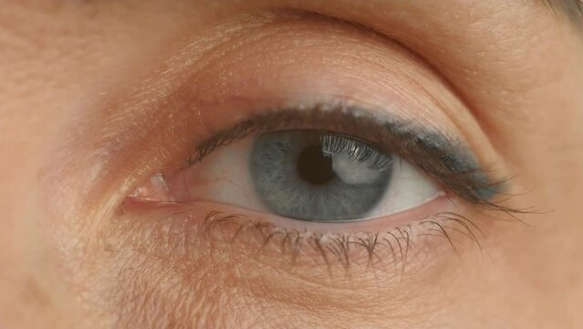 Opening woman left eye close up. Eyelids with eyelashes and facial skin of middle aged female. Human vision, eye pupil and iris, blood vessels, anatomical structure of eyeball macro