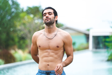 Fototapeta premium Feel the sun and music by the pool. A handsome man is refreshing in the pool water and listening to his favorite song. Swimming and sunbathing, hot summer day and enjoying summer days and rest
