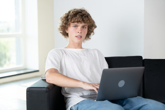 Young curly-haired student sitting on couch, working diligently on laptop at home. The cozy atmosphere suggests a productive study session.