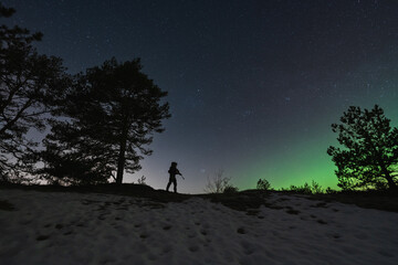 Naklejka na ściany i meble A soldier with a night vision device and a rifle with a silencer in the forest against the background of the starry sky and northern lights.