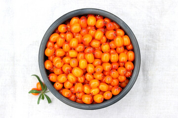 Ripe sea buckthorn berries in the black ceramic bowl on aged wood, linen, background