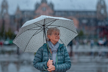 Senior woman walking in the city in a rainy day holding an umbrella while strolling outside. Copy...