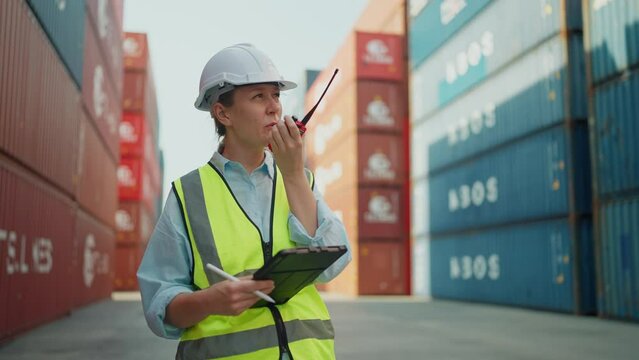 Cuacasian woman industrial engineer talking on walkie talkie or radio processes orders and product at warehouse logistic in cargo freight ship for import export in harbor. Import and export product