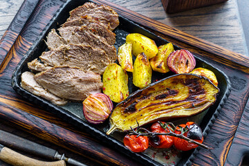 Grilled vegetables with meat on a cast iron trey on table above - 750437936