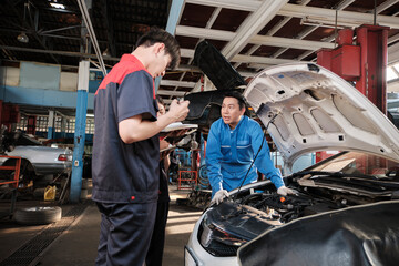 Asian male professional automotive engineer supervisor describes car engine maintenance and repair work with mechanic worker staffs team in fix service garage, specialist occupations in auto industry.