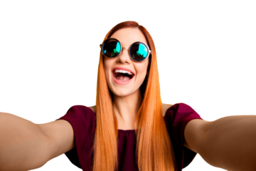 Close up portrait of silly mad girl in glasses with beaming smile making selfie on front camera of smartphone isolated on yellow background