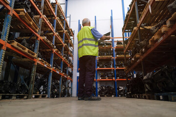Senior auto mechanic taking standing amidst shelves at warehouse