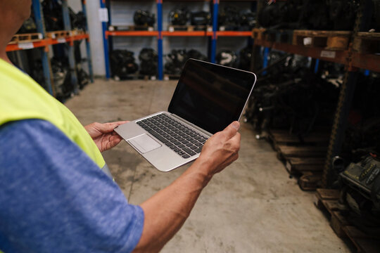 Senior auto mechanic holding laptop at warehouse