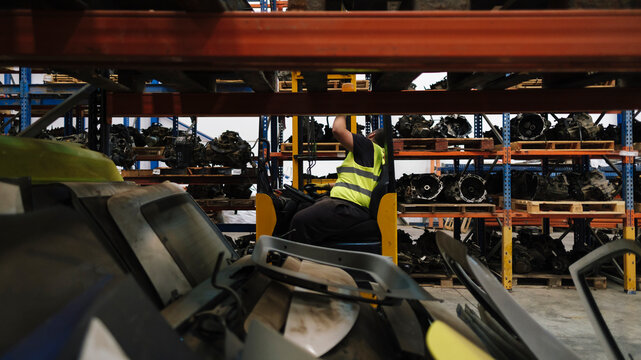 Mechanic sitting in forklift near shelves at warehouse
