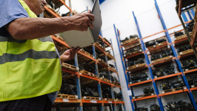 Auto mechanic taking inventory of vehicle parts using laptop at workshop