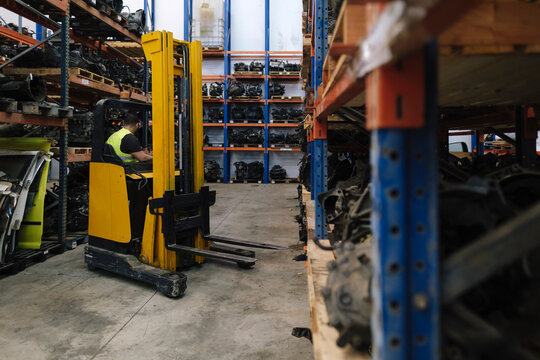 Mechanic operating forklift near shelves at warehouse