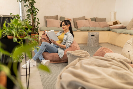 Businesswoman reading book relaxing on bean bag at co-working space