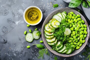 Healthy vegan green avocado salad bowl with sliced cucumbers, edamame beans, olive oil and herbs on ceramic plate top view on grey stone rustic table background. 