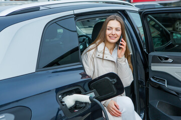 
Young business woman refueling her electric car at a EV charging station. Concept of environmentally friendly vehicle. Electric car concept. Green travelling.
