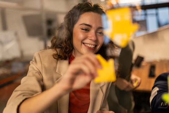 Smiling businesswoman sticking adhesive notes on glass wall at home