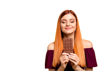 Cute red-haired young woman with pleasure and dreaminess holds a chocolate in her hands isolated on...