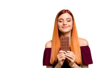 Cute red-haired young woman with pleasure and dreaminess holds a chocolate in her hands isolated on yellow background with copy space for text