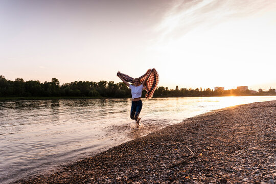 Happy woman holding blanket and running at beach