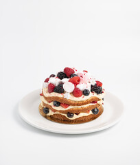 Cake layered with cream and decorated with fresh berries and marshmallows, on a white plate on an isolated background.