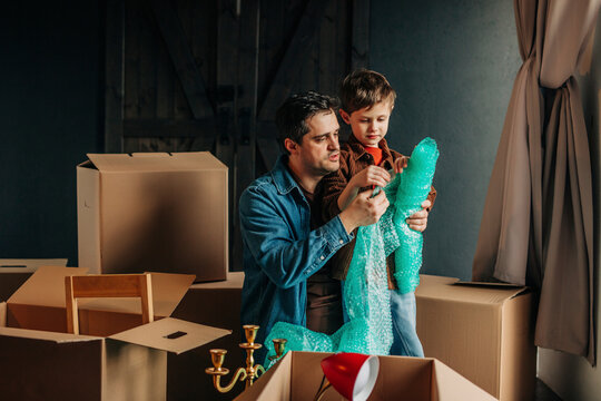 Father with son holding roll of bubble wrap near cardboard boxes