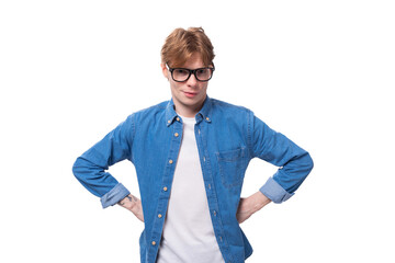 portrait of a slender handsome european red-haired student guy dressed in a denim shirt and glasses on a white background