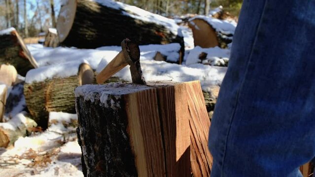 Close up and slow motion while using wood block hitting ax head used as wedge stuck in oak stump and splitting log into smaller pieces.