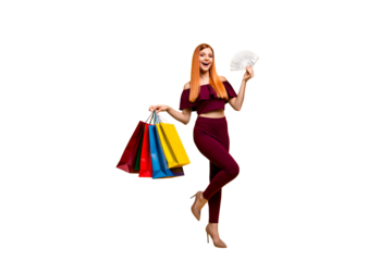 Full length size body portrait of red straight-haired beautiful young girl, wearing suit, pants, top blouse, holding shop bags and fan of dollars cash. Isolated over bright vivid yellow background