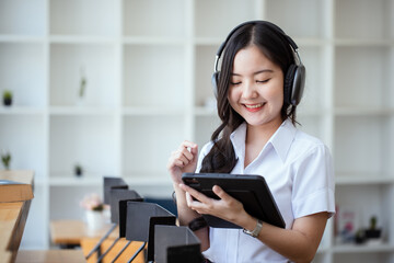Naklejka premium Happy young asian woman wearing earphones and using tablet at desk in office, Female asian student with digital tablet, College female student learning online.