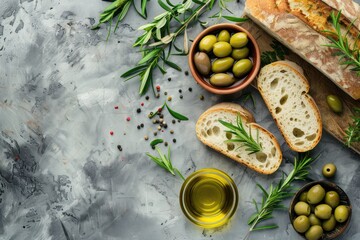 Slices of fresh ciabatta, green and brown olives, olive oil with rosemary, olive tree branches on gray concrete stone rustic background overhead