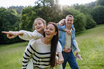 Portrait of beautiful family, parents piggibacking two daughters, having fun in nature.