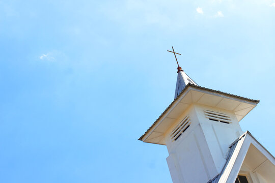 White church tower with cross against blue sky background in sunny weather