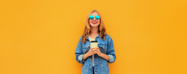 Beautiful happy smiling young woman with cup of coffee in denim jacket on yellow background