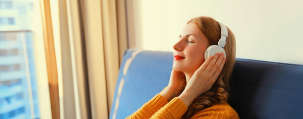 Happy relaxed young woman listening to music with headphones lies on couch at home