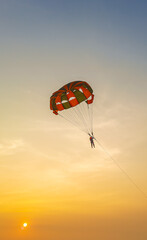 Parasailing extreme sports on beach in sunset background. Paragliding in front of an amazing sunset. A beautiful background of a parasailing parachute on the backdrop a sunset on an evening sky.