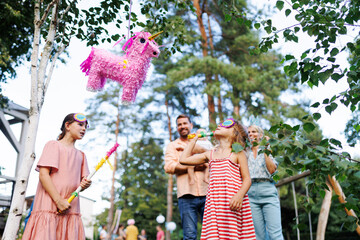 Two girls smashing, hitting pinata with a stick at birthday party. Children celebrating birthday at garden party. Children having fun and playing.