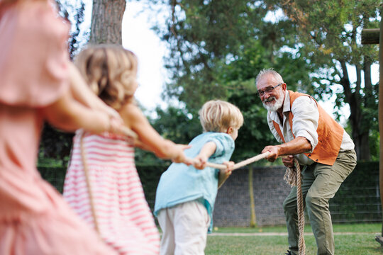 Grandfather has a tug of war with their grandkids. Fun games at family garden party.