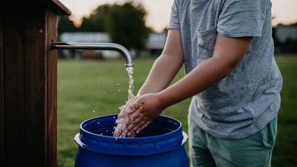 Boy washing his hands with water from a well. Well with a pump for outdoor washing in garden.