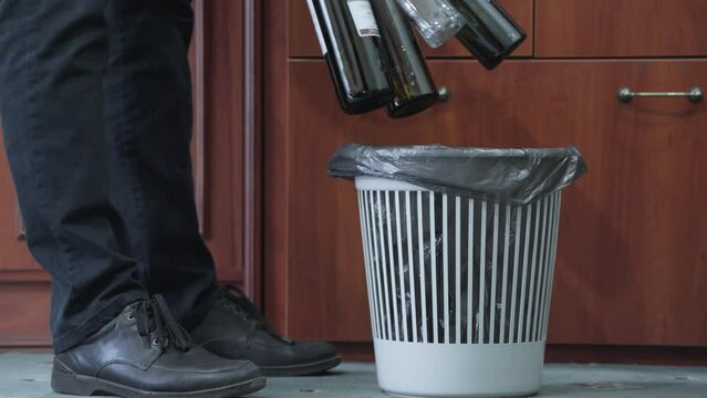 Man throws empty alcohol bottles into trash bin.