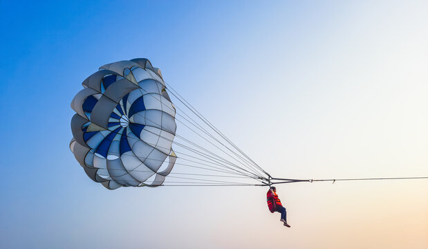 Parasailing extreme sports on beach in blue sky background. Man is parasailing in the blue sky. Paragliding in the clear sky above the sea.