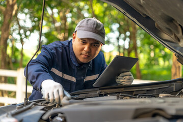 Asian automobile mechanic repairman wearing uniform and protection glove repairing a car engine automotive workshop with tablet, car service and maintenance, Repair service.