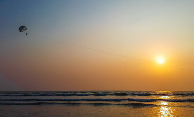 Parasailing extreme sports on beach in sunset background. Paragliding in front of an amazing sunset. A beautiful background of a parasailing parachute on the backdrop a sunset on an evening sky.