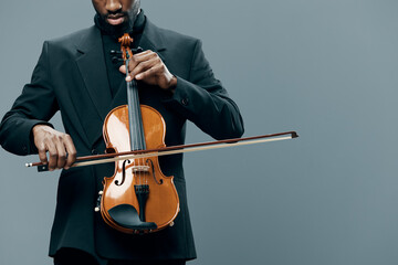 Elegant African American Man Playing Violin in Tuxedo on Gray Background in Studio Setting